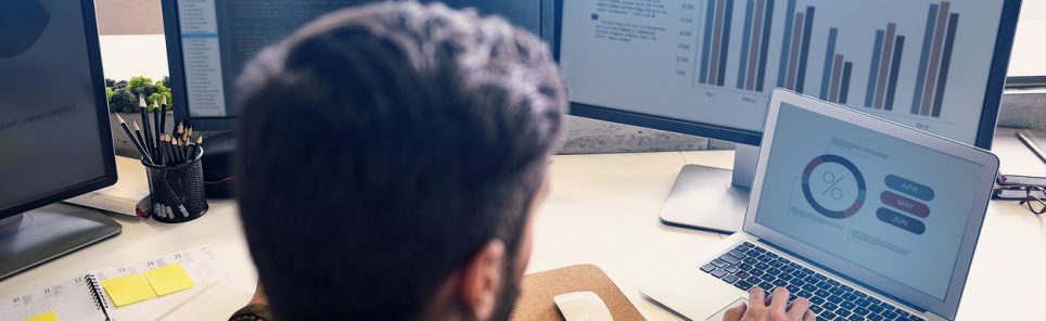 Man creating statistics in modern office. He working on digital devices while sitting at table and turning back to camera