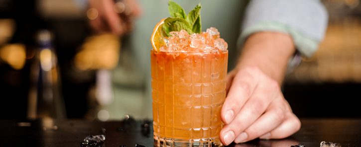 Bartender finished decorating his cocktail with mint and orange slice