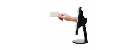 A hand holding a blank card towards a sideways computer monitor on a white background.