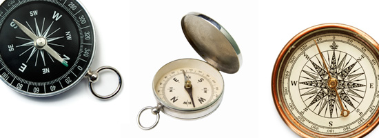 Three compasses in a row, including a modern black and white compass, a vintage pocket compass with a metallic case, and an ornate antique compass with detailed designs.