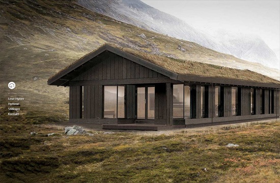 A modern dark wood cabin with large windows located in a grassy mountainous landscape with misty mountains in the background.