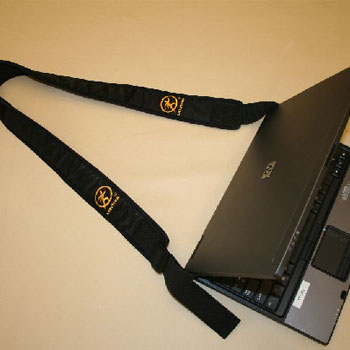 A black martial arts belt with gold embroidery lying next to a partially closed black laptop on a table.