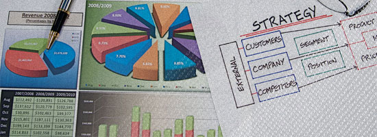 Printed business charts and a handwritten strategy note. The charts include a pie chart detailing revenue distribution by region for 2008/2009 and a bar graph showing multi-year revenue trends. The strategy note outlines external factors such as customers, company, and competitors, with subcategories for business planning.