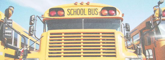 Front view of a yellow school bus with the words 'SCHOOL BUS' above the windshield, surrounded by a clear sky and parts of other buses.