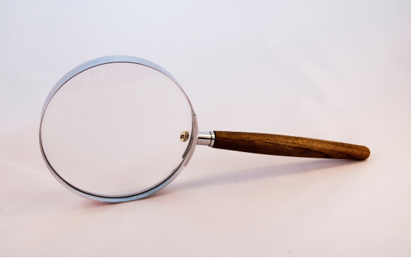 A classic magnifying glass with a round lens and a wooden handle on a light-colored surface.