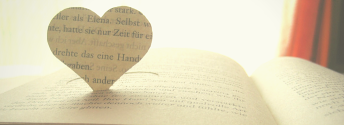 An open book with its pages folded into a heart shape, illuminated by soft sunlight.