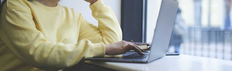 Person in a yellow sweater working on a laptop at a desk.