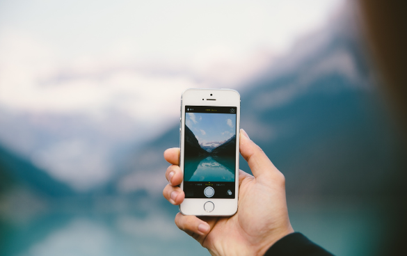 A hand holds a phone in front of a lake to take a photo