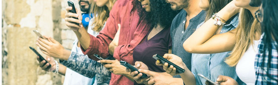 A diverse group of people standing in a row, each engrossed in their own smartphone, highlighting a common social scene of technology use.