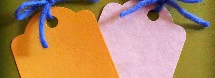 Two blank scalloped tags, one orange and one pink, with blue yarn, on a green surface.