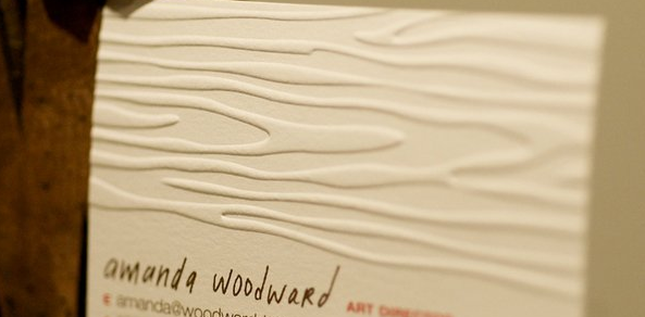 Close-up of a textured business card with embossed wavy lines, featuring the name 'amanda woodward' and the title 'ART DIRECTOR'.