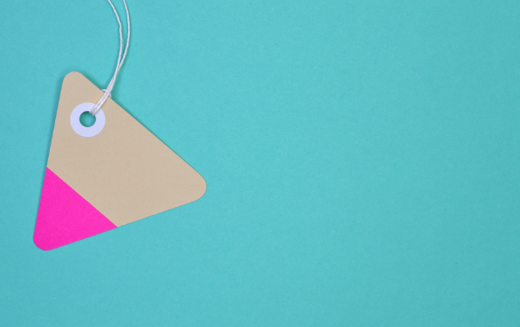 A triangular paper price tag with a pink corner on a turquoise background, with a white string looped through a reinforced hole.