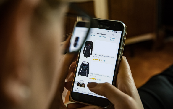 Person holding a Samsung smartphone displaying an online shopping page with a black jacket, showing price and customer ratings.