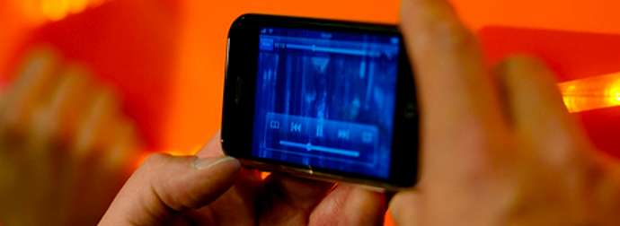 Person holding a smartphone with a digital audio interface displayed on the screen, against an orange background.