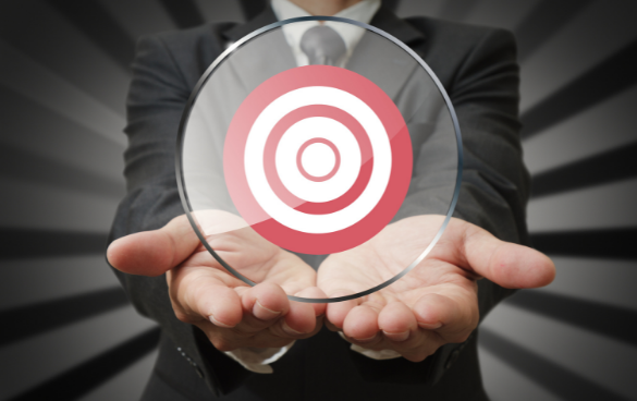 Person in a business suit holding a transparent disc with a red and pink target symbol centered on it, against a radial gray background.