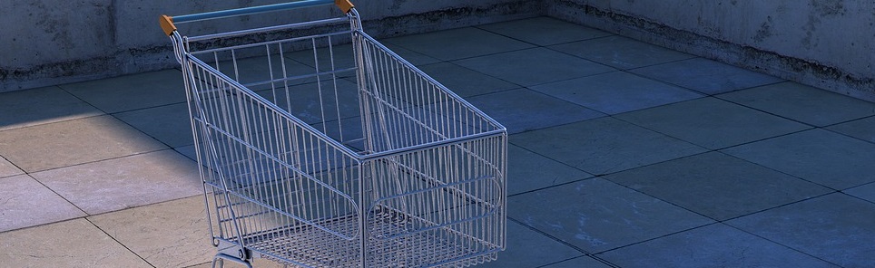 An empty metal shopping cart on a tiled floor with walls in the background, suggesting an outdoor setting.