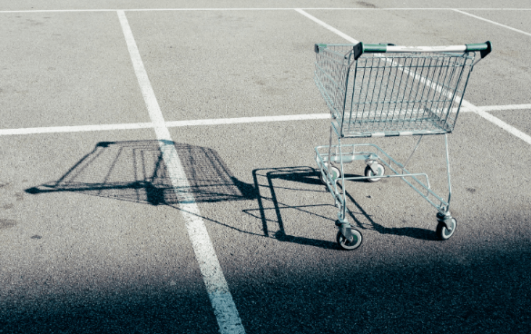 A metal shopping cart in a parking lot casting a sharp shadow on the pavement.