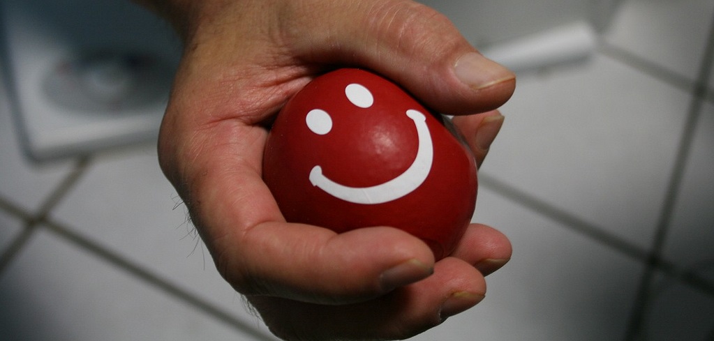 A person's hand holding a red egg with a white smiley face, against a tiled background.