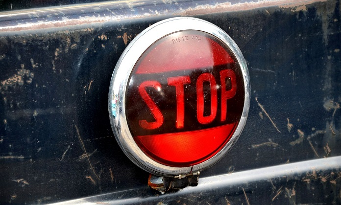 Vintage round stop light with a red lens and the word 'STOP' on a dirty and scratched vehicle surface.