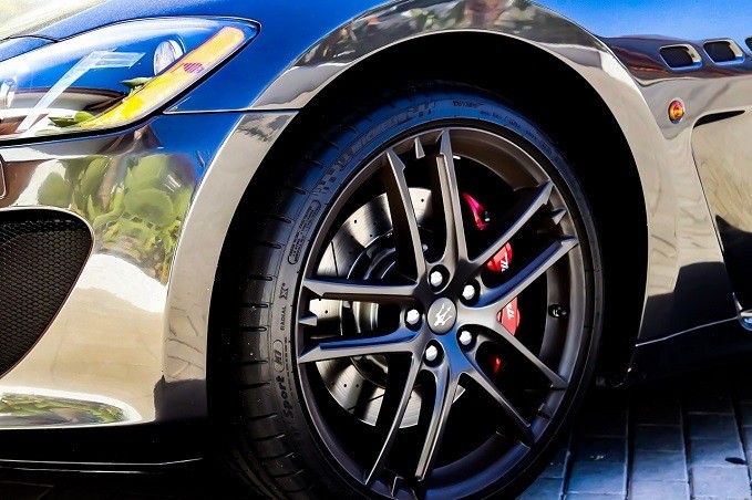 Close-up of a Maserati car's wheel with a black multi-spoke rim, red brake caliper, and Pirelli tire, reflecting a well-polished metallic body.