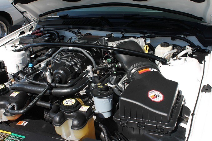 Close-up view of a clean and organized car engine bay with labeled fluid reservoirs and a performance badge on the engine cover.