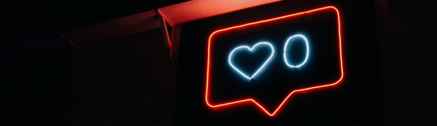 Neon sign with a heart and zero symbols inside a red speech bubble outline against a dark background.