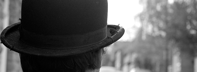 Rear view of a person wearing a worn top hat with a frayed brim, with an out-of-focus outdoor background.