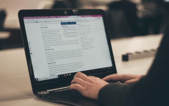 Person typing on a laptop with a document displayed on the screen in an indoor setting.