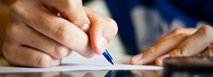 Close-up of a right-handed person writing on paper with a blue pen, wearing a blue sleeve.