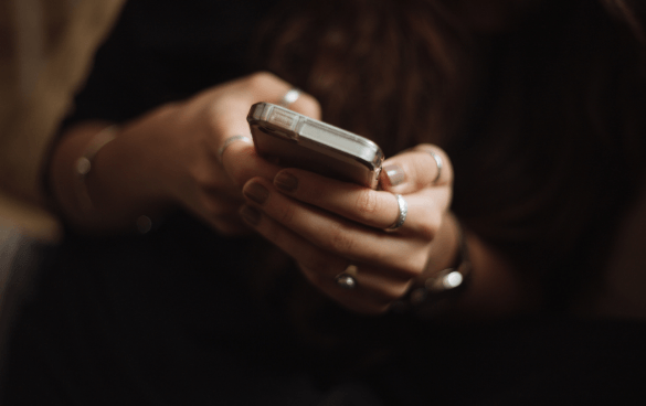 Close-up of a person's hands with rings holding and using a smartphone.