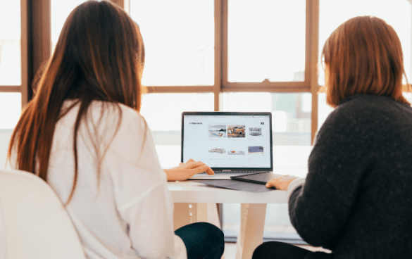 Two women collaborating at a table with a laptop in a well-lit room.