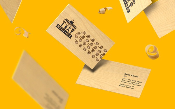 Wooden stamp with a building icon and button grid design, a business card for Rune Cohle, and wood shavings on a yellow background, implying stamping or carving activity.