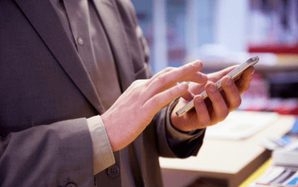 A person in a business suit using a smartphone with a blurred indoor background.