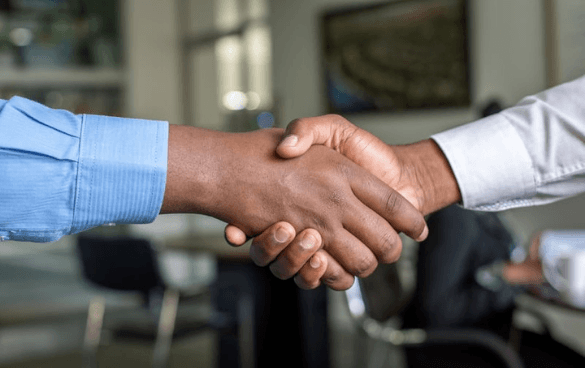 Two people in long-sleeved shirts shaking hands in an office setting.