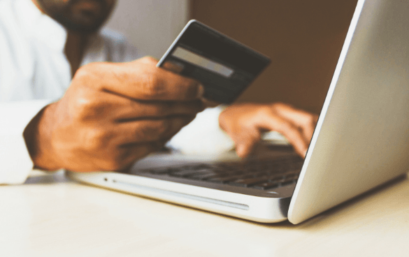 Person holding a credit card while typing on a laptop, likely making an online purchase.