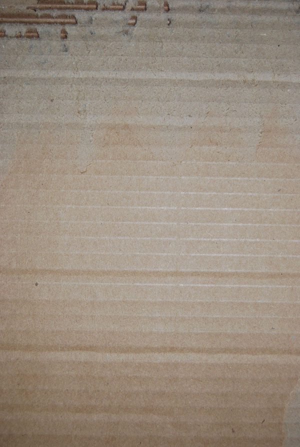 Close-up of a piece of light brown corrugated cardboard with a torn edge exposing the inner texture.