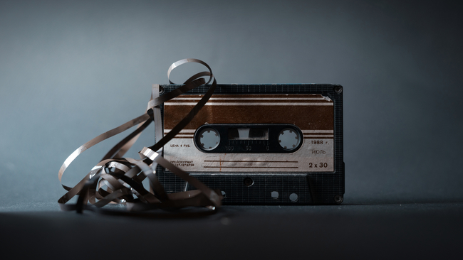 A vintage cassette tape with its magnetic tape unwound and tangled, set against a dark grey background.