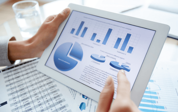 Person analyzing data on a tablet with charts and graphs, with a printed spreadsheet in the foreground.