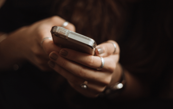 Close-up of a person's hands with rings, holding and using a smartphone with a clear case.