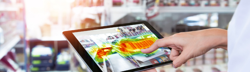 A person's hand holding a tablet displaying a heat map overlay on a retail store layout.