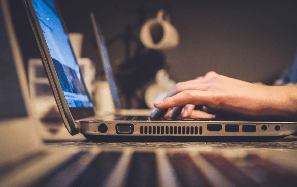 Close-up of a person's hand on a laptop keyboard with a softly lit indoor background.