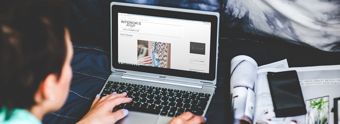 Person browsing an interior design website on a laptop with an open magazine beside them, indicating research or work on interior decorating.