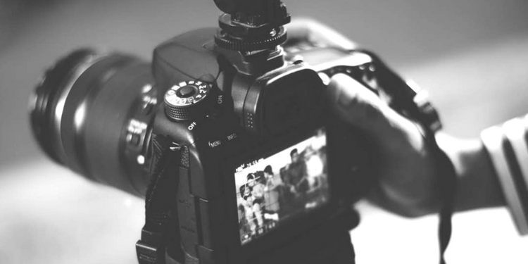 A black and white photo of a DSLR camera with its screen displaying a group of people.