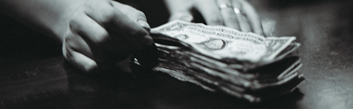 Close-up of a hand holding a stack of US dollar bills.