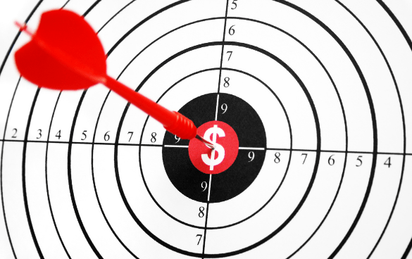 A dart is stuck in the bullseye of a dartboard, which features a dollar sign symbol in the center, symbolizing financial success or monetary target achievement.