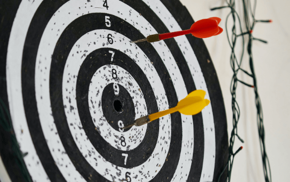 Two arrows in an archery target, one red arrow in the outer white ring and one yellow arrow in the bullseye.