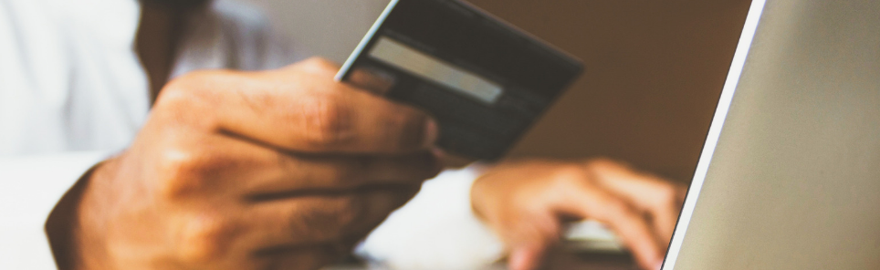 Person holding a credit card while typing on a laptop, indicating an online transaction or shopping activity.