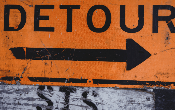 Weathered orange detour sign with bold black text and a right-pointing arrow.