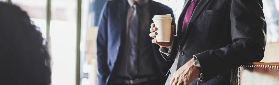 A person in a business suit holding a disposable coffee cup, with a blurred background suggesting a professional setting.