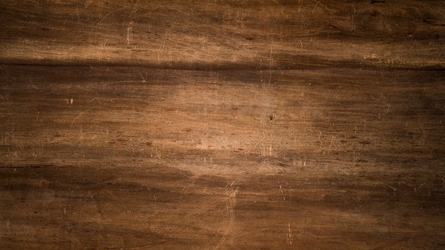 Close-up of a rustic wooden surface with visible grain, scratches, and aged textures.